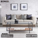 A modern coffee table with a clear glass top, black steel frame, and a wooden shelf underneath. The table is placed in a living room setting with a sofa and cushions in the background.